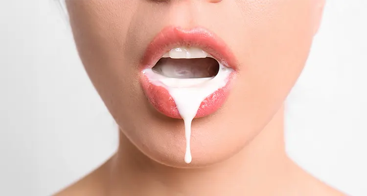 Lips of a woman standing in front of white background with a while sticky liquid dripping from her mouth.