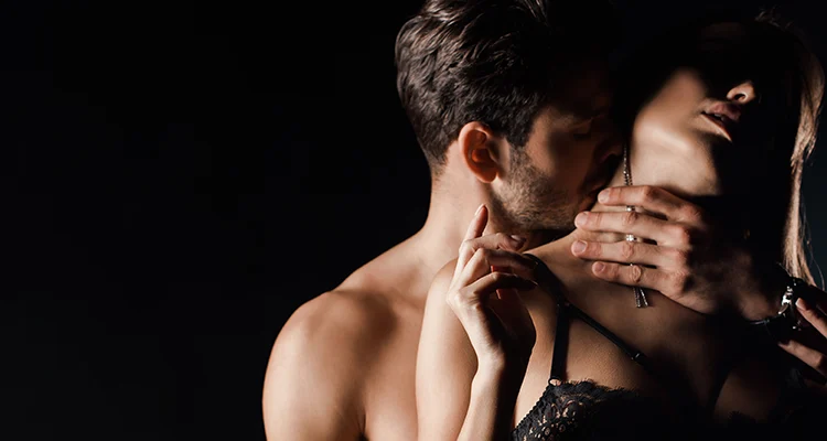 Brunette shirtless man kissing the neck of a brunette woman in black lace bra while holding her by the neck.