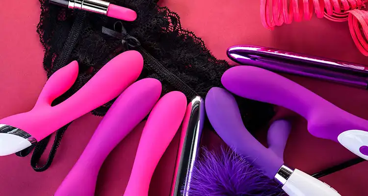 Pink and purple vibrators and dildos on pink background with black lacy underwear and pink lipstick.