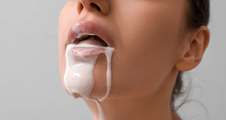 Brunette woman looking upwards with her mouth half opened and a white liquid dripping down from it to her chin.