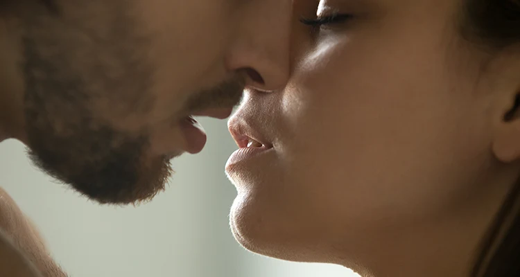 Brunette man with a stubble leaning in to kiss a brunette woman who has her eyes closed.