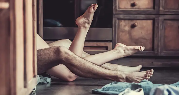 Naked legs of a man and woman lying on the floor with clothes all around them, covered by a door.
